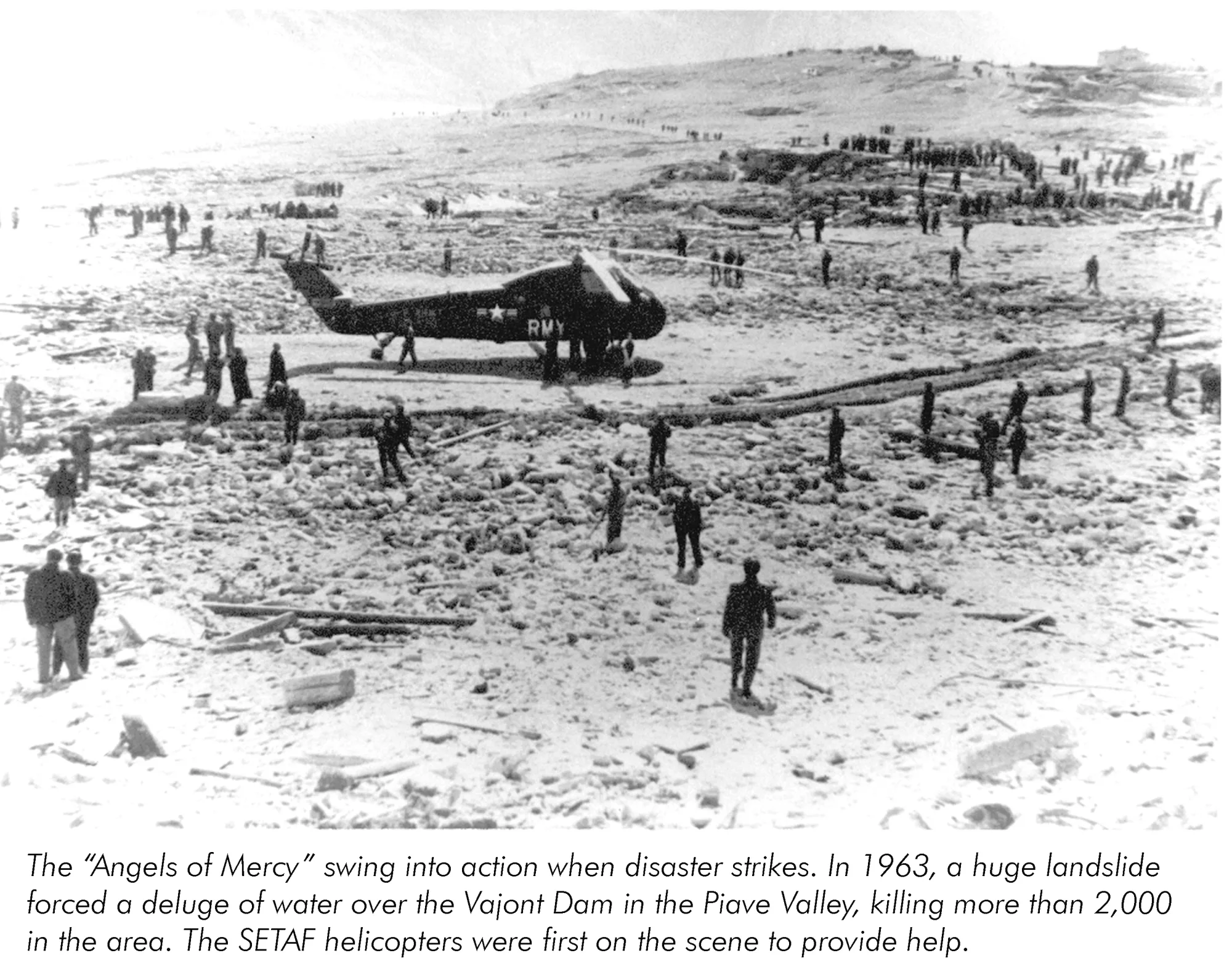 Foto histórica em preto e branco de um helicóptero e pessoas entre destroços após o desastre de Vajont.